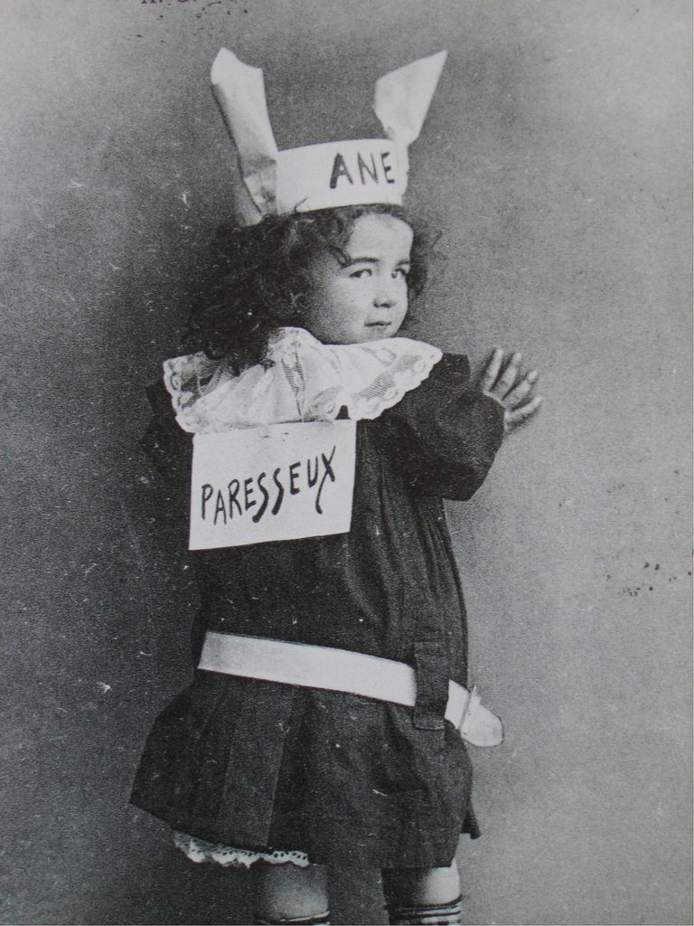 Enfant avec un bonnet d'âne et une pancarte "paresseux" dans le dos.